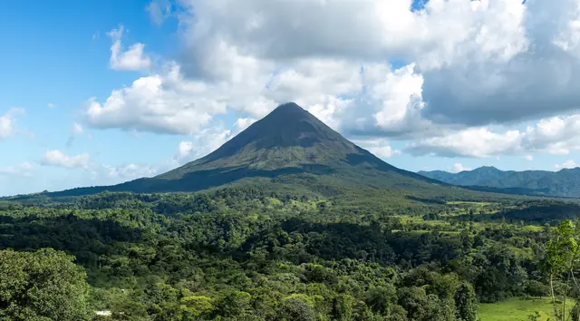 Volcán Arenal con su cono perfecto sobre el bosque y cielo con nubes