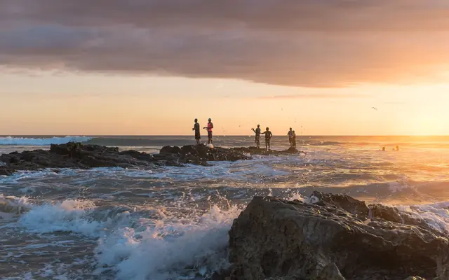 Pescadores sobre las rocas al atardecer en Playa Santa Teresa